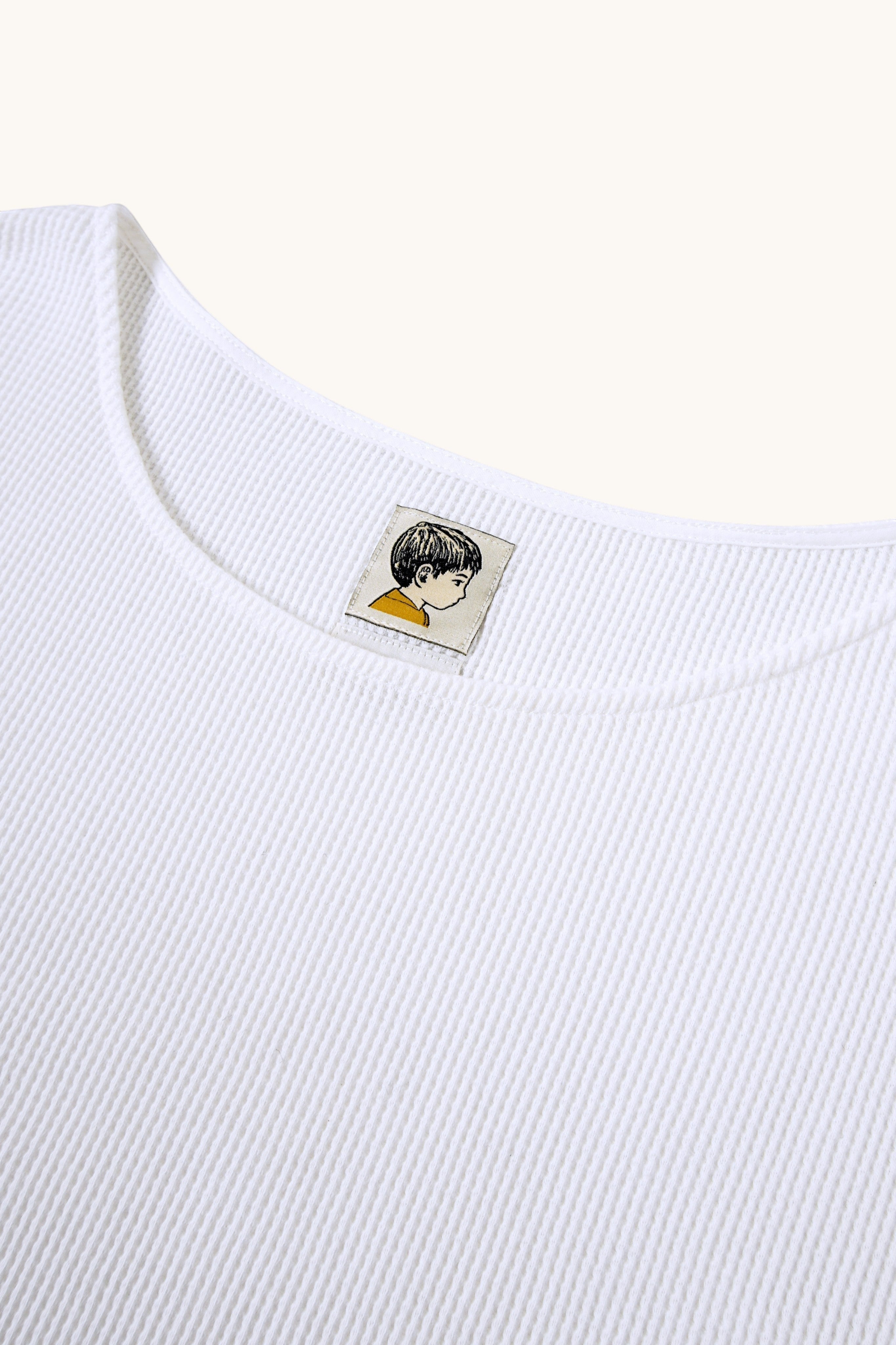MEG.S white 100% cotton waffle knit long sleeve shirt with a wide neckline and graphic tag.